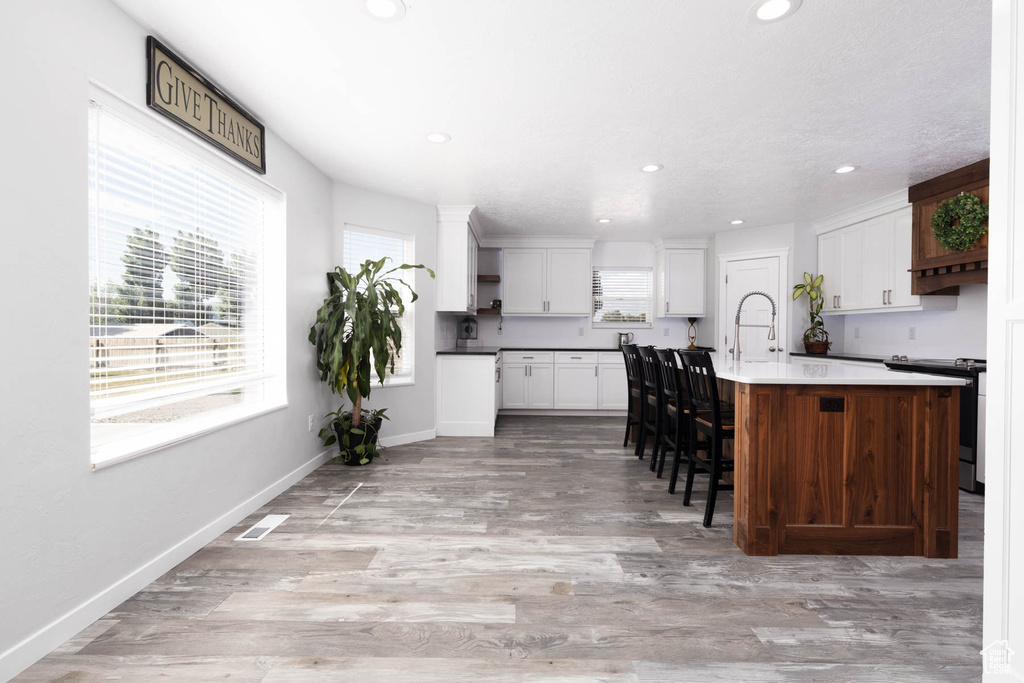Kitchen with stainless steel electric stove, recessed lighting, light wood finished floors, white cabinets, and a breakfast bar area