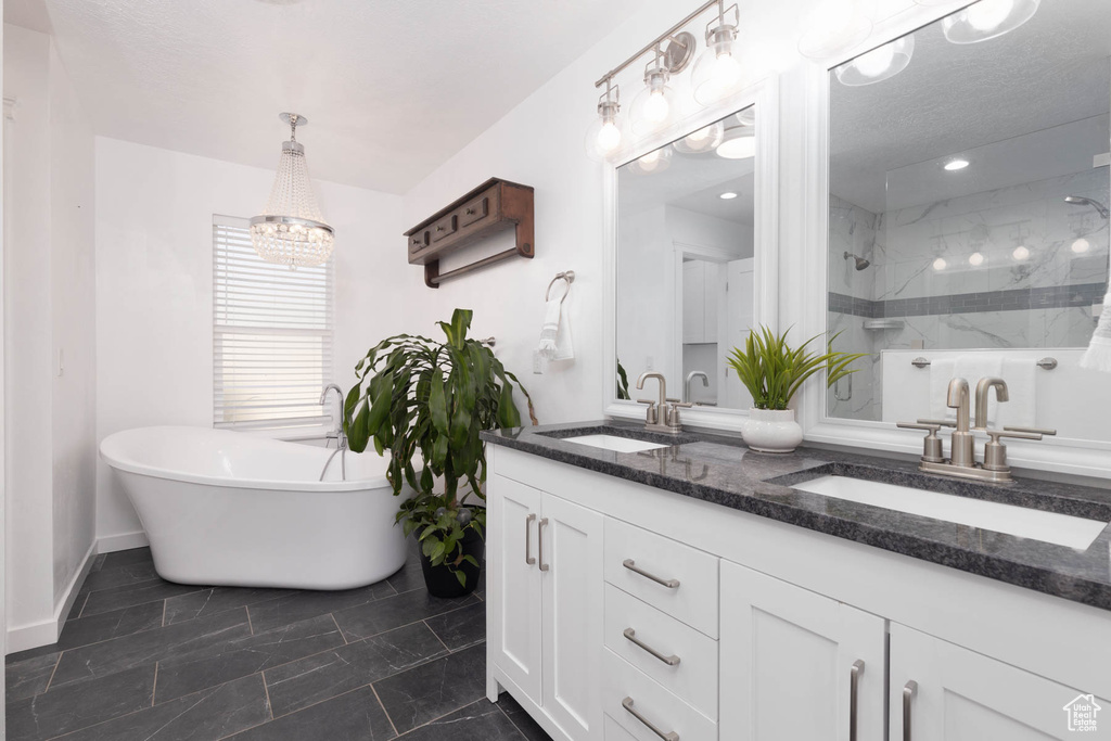Bathroom with double vanity, a stall shower, a freestanding bath, a chandelier, and baseboards