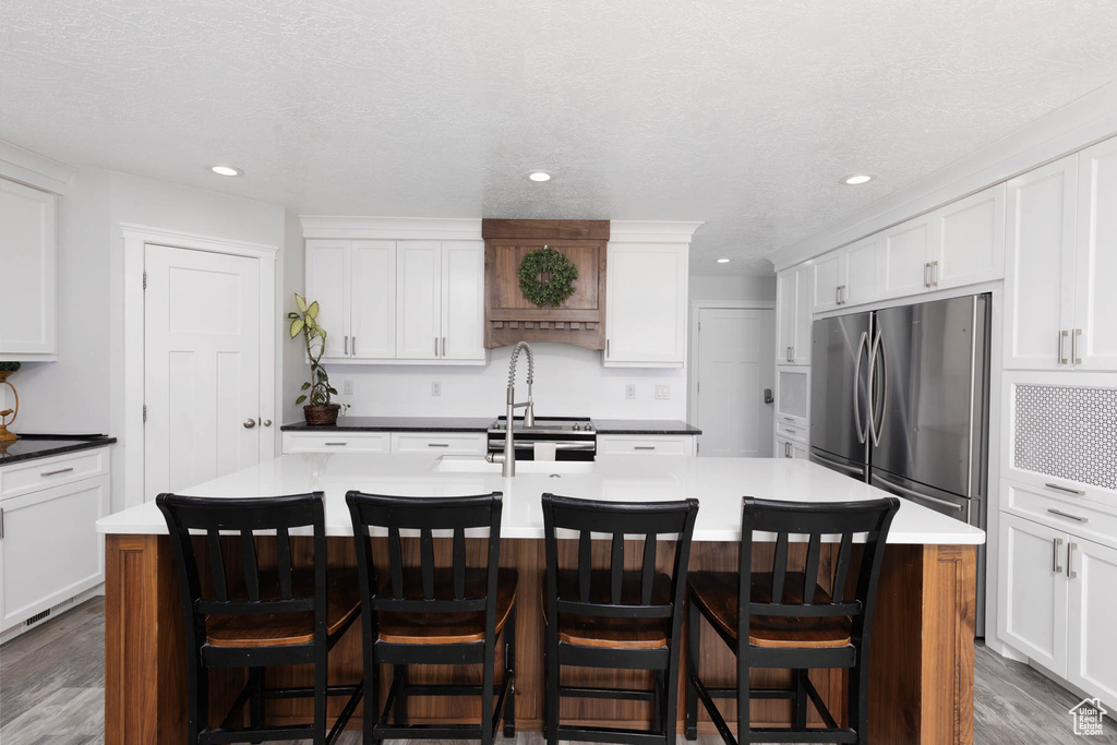 Kitchen featuring appliances with stainless steel finishes, wood finished floors, a center island with sink, white cabinets, and recessed lighting