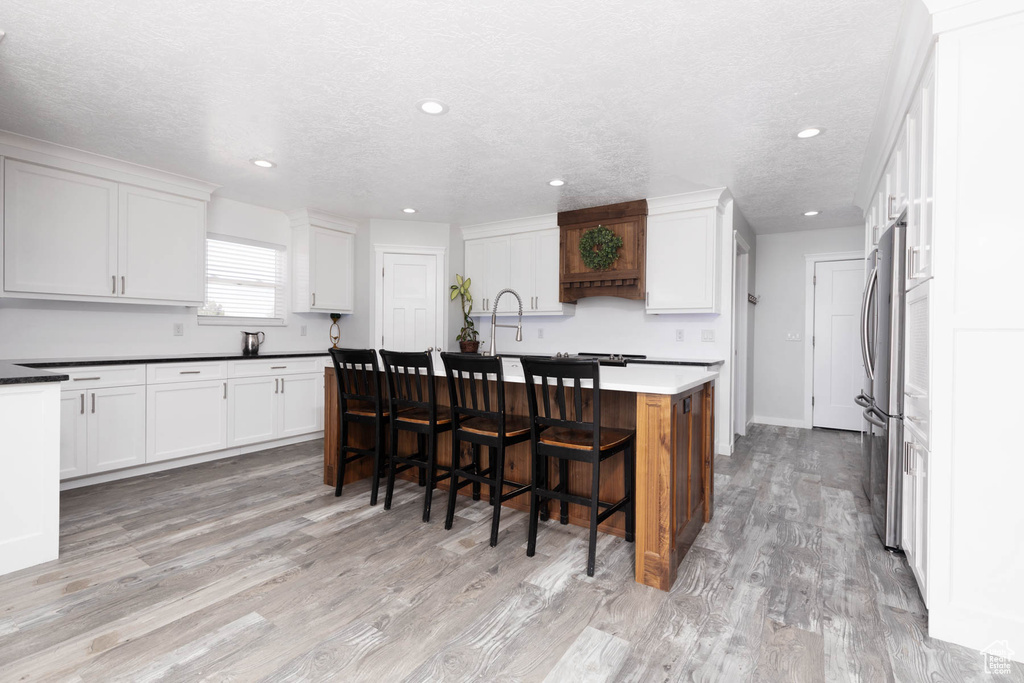 Kitchen featuring freestanding refrigerator, white cabinets, light wood-style floors, a breakfast bar, and a kitchen island with sink