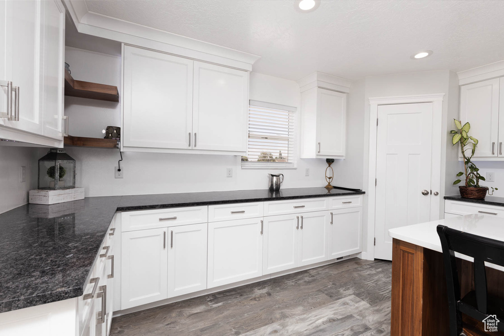 Kitchen with open shelves, white cabinets, wood finished floors, recessed lighting, and dark stone countertops