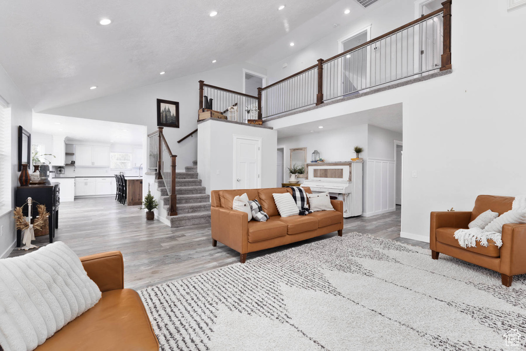 Living area featuring high vaulted ceiling, stairway, light wood-type flooring, recessed lighting, and baseboards