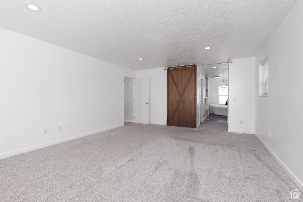 Unfurnished bedroom with a barn door, recessed lighting, carpet, a textured ceiling, and baseboards