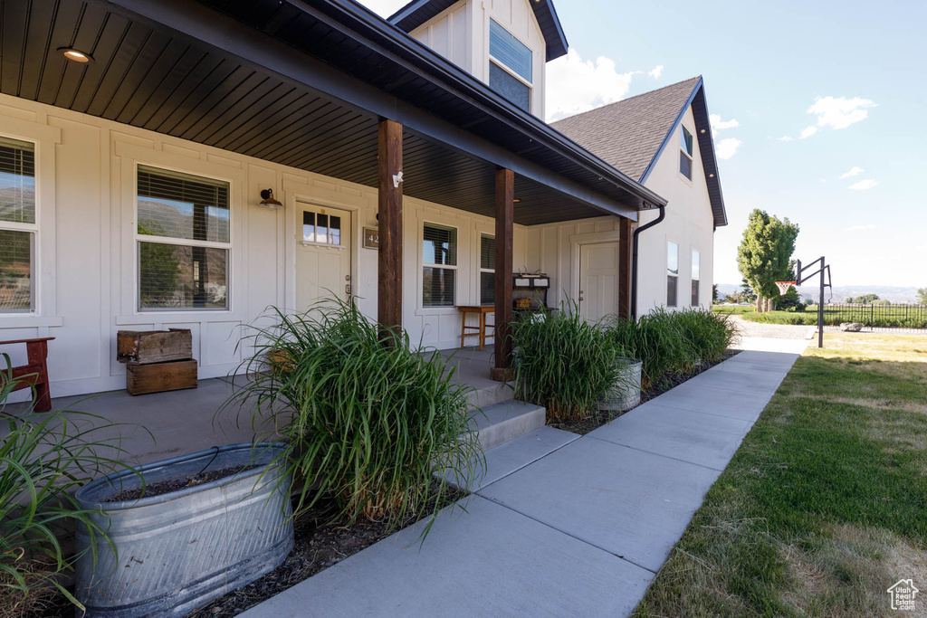 View of exterior entry with covered porch, a shingled roof, and board and batten siding