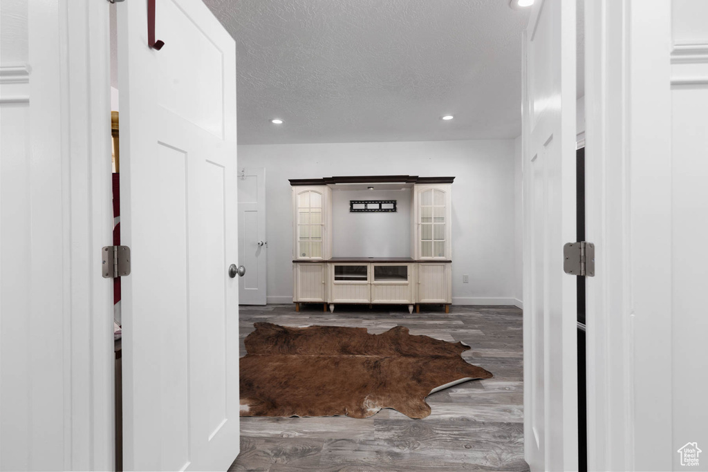 Hall with wood finished floors, recessed lighting, baseboards, and a textured ceiling