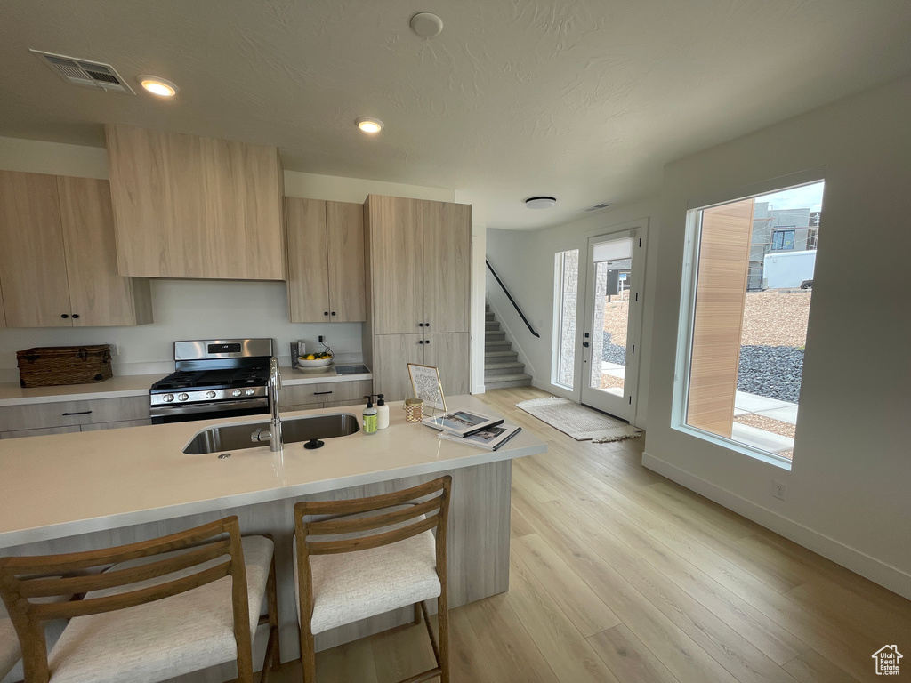 Kitchen featuring gas range, light brown cabinetry, a sink, modern cabinets, and light countertops