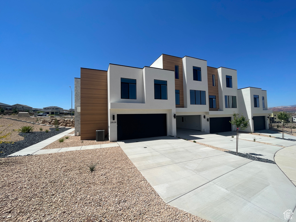 Modern home featuring a garage, stucco siding, driveway, and central air condition unit