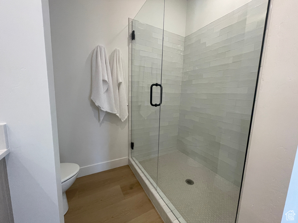Full bathroom with wood finished floors, toilet, a shower stall, and baseboards