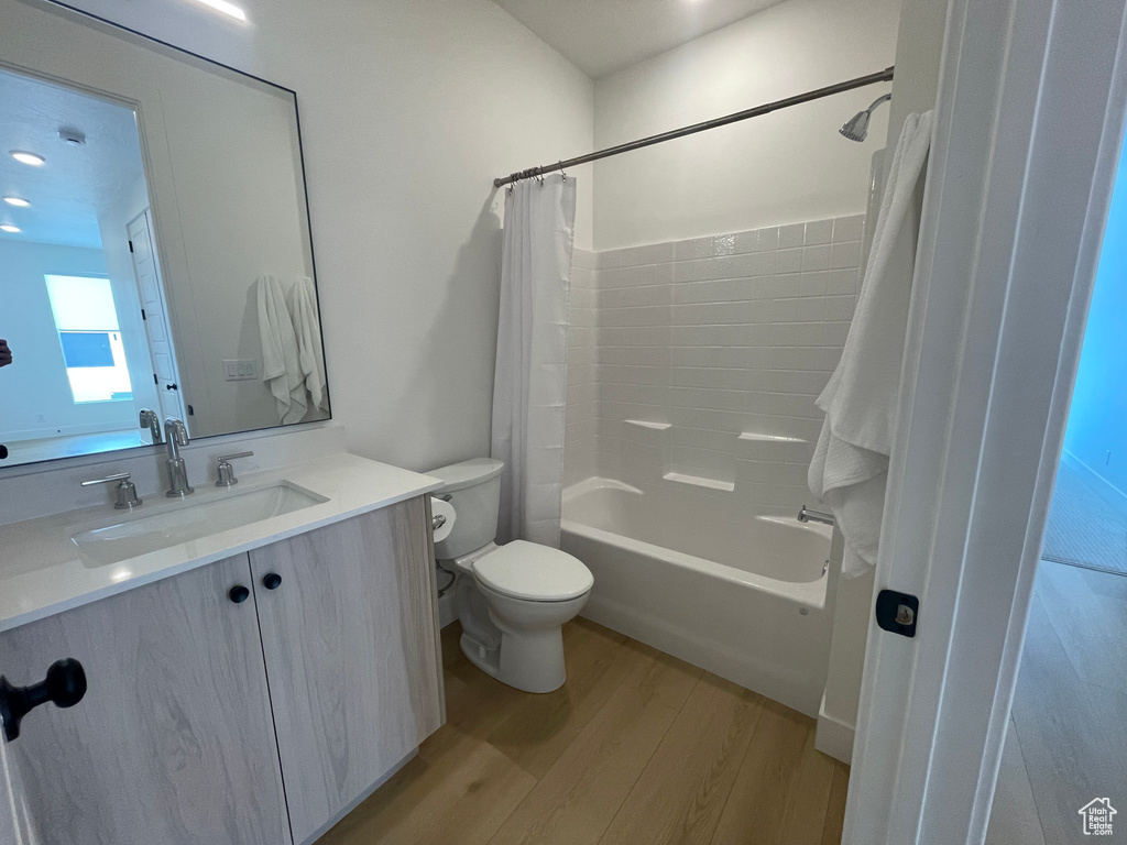 Full bathroom featuring wood finished floors, vanity, toilet, and shower / bathtub combination with curtain