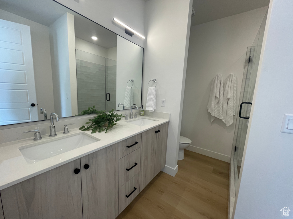 Bathroom featuring toilet, double vanity, a stall shower, wood finished floors, and baseboards