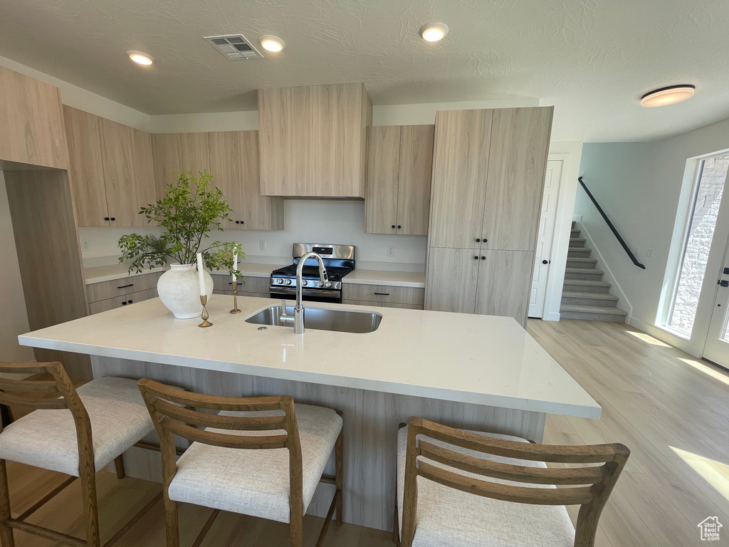 Kitchen with a sink, light brown cabinetry, modern cabinets, a breakfast bar area, and recessed lighting