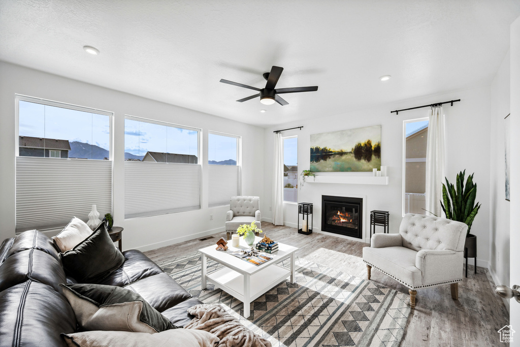 Living room with ceiling fan, wood finished floors, a glass covered fireplace, baseboards, and recessed lighting