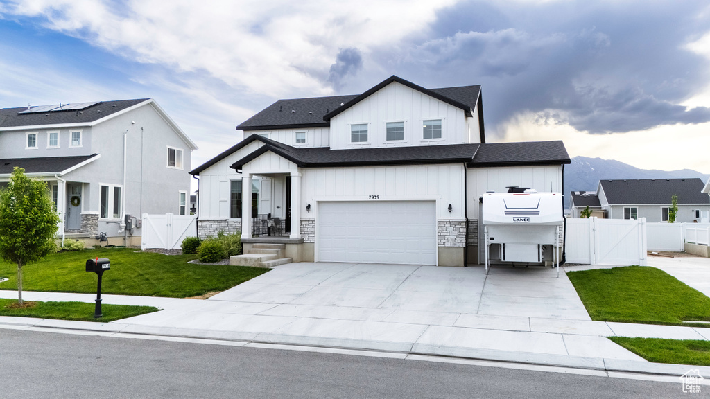 Modern farmhouse style home with a gate, board and batten siding, an attached garage, driveway, and stone siding