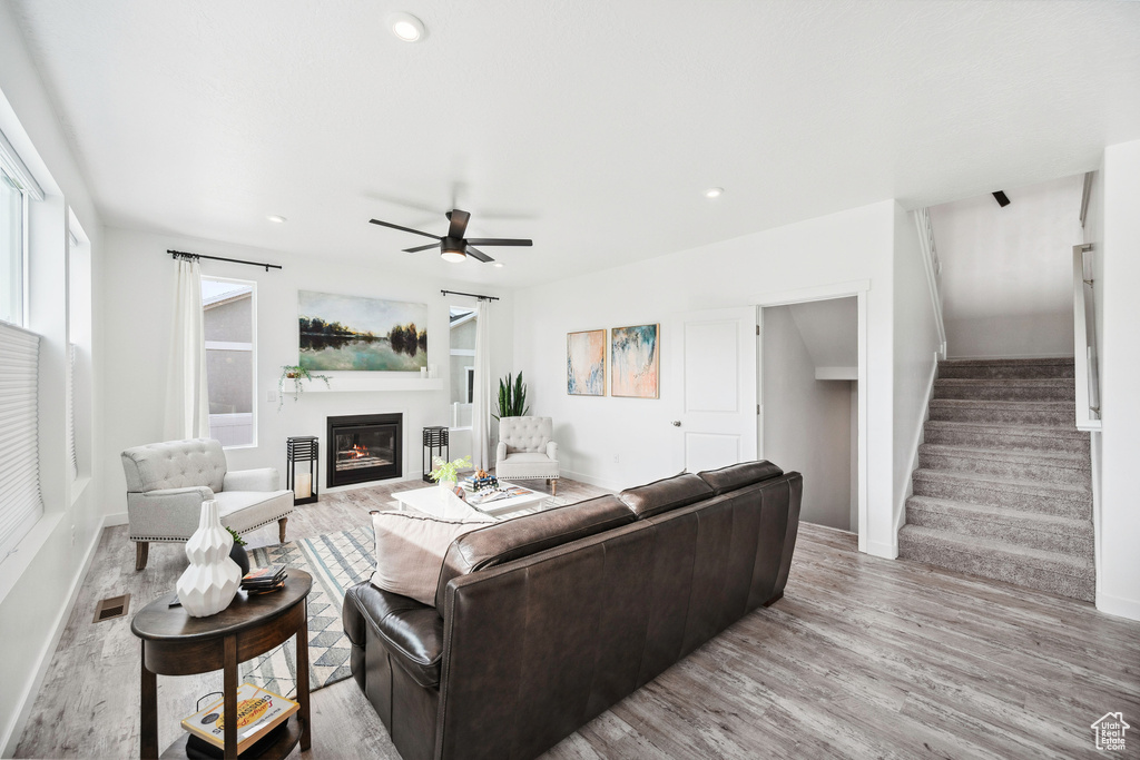 Living area with a glass covered fireplace, light wood-style flooring, stairs, baseboards, and recessed lighting