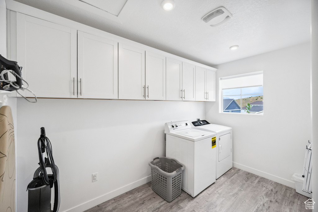 Laundry room featuring separate washer and dryer, cabinet space, baseboards, and light wood finished floors