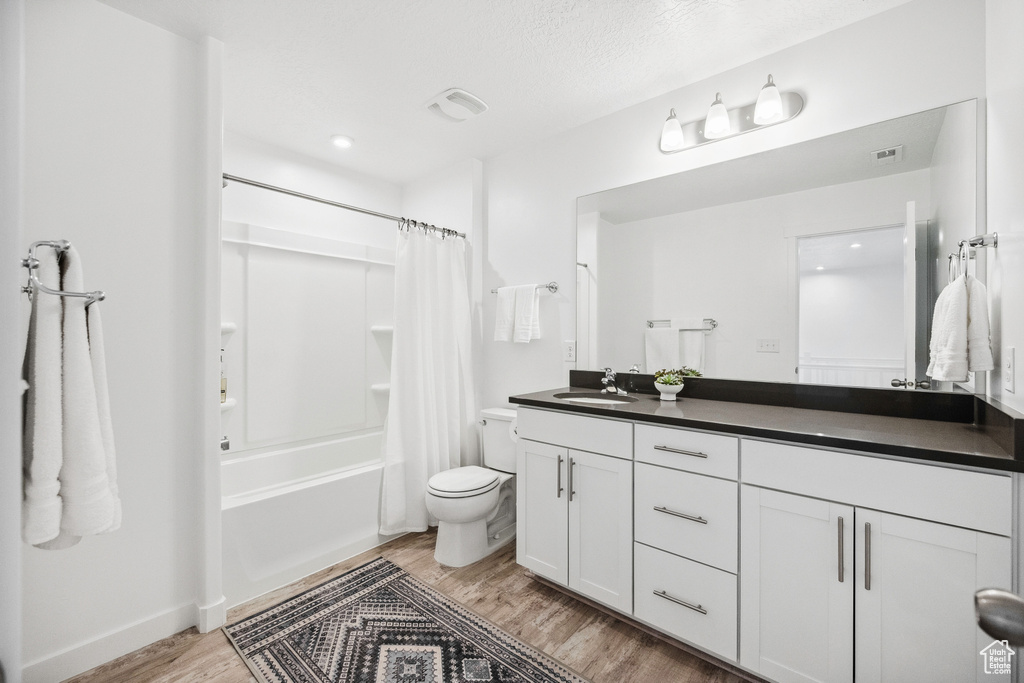 Full bath featuring wood finished floors, double vanity, toilet, shower / bath combo with shower curtain, and recessed lighting