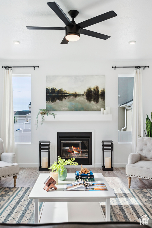 Living area with ceiling fan, a glass covered fireplace, baseboards, wood finished floors, and recessed lighting