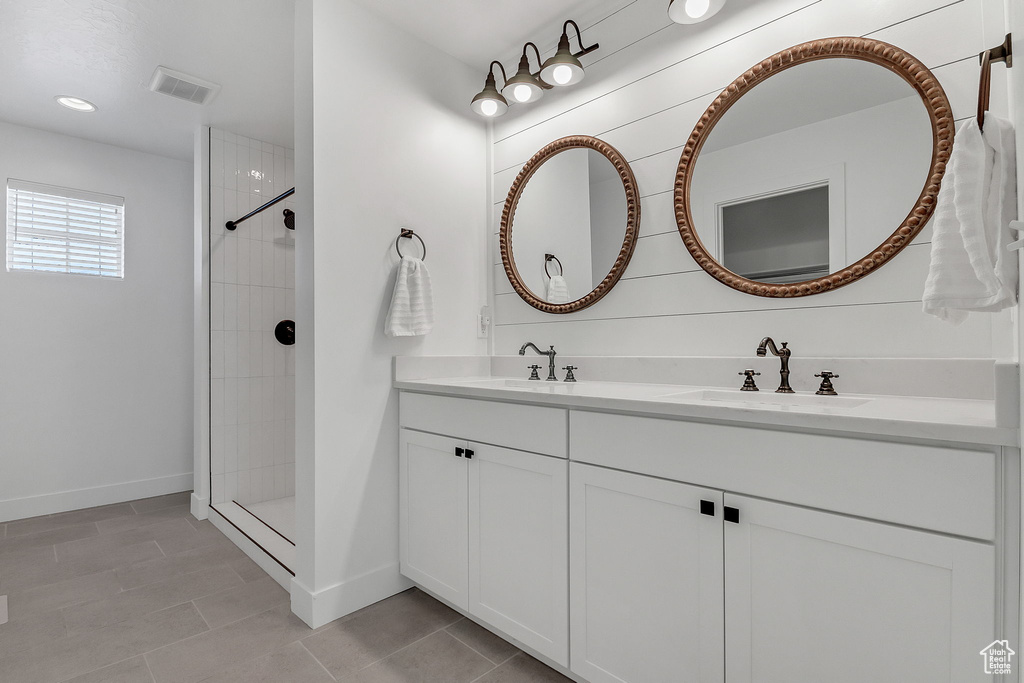 Full bath featuring double vanity, tiled shower, and baseboards