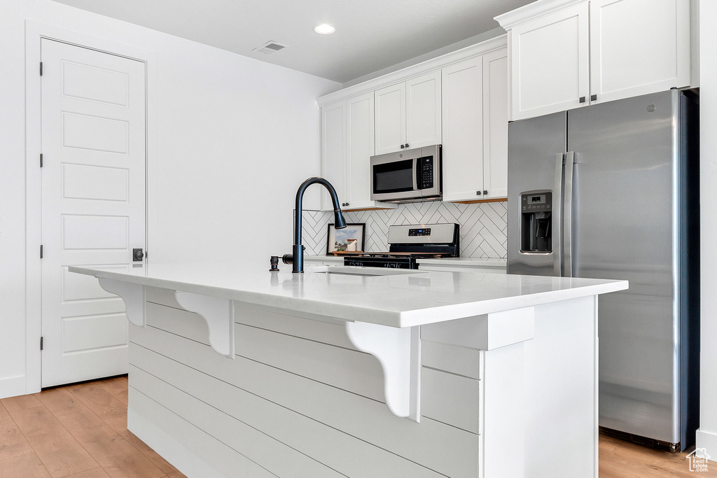 Kitchen with appliances with stainless steel finishes, white cabinets, light wood-style floors, and recessed lighting