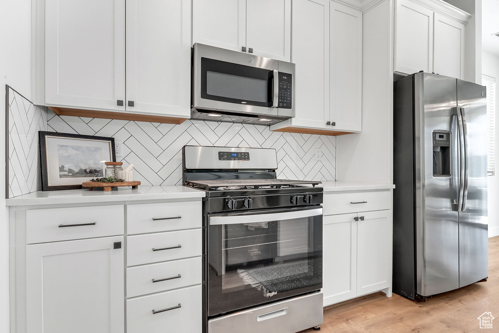 Kitchen featuring stainless steel appliances, light countertops, white cabinets, light wood-type flooring, and decorative backsplash