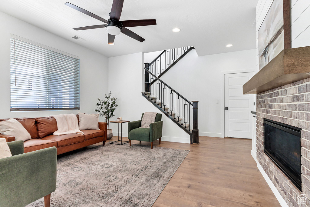 Living area with a fireplace, stairway, ceiling fan, wood finished floors, and baseboards