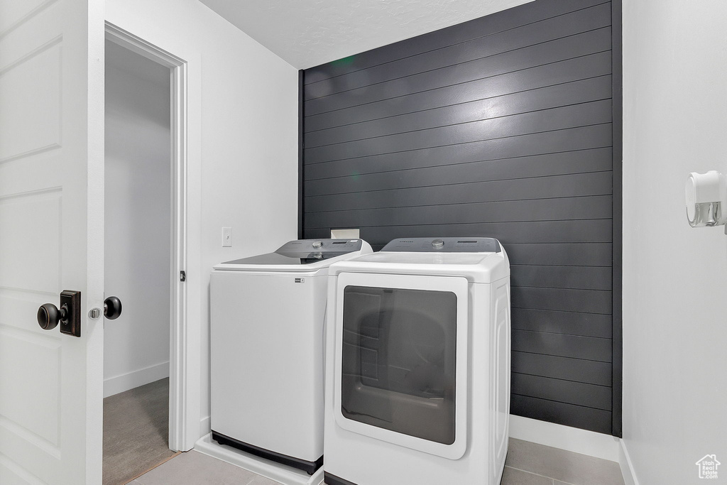 Laundry room with washer and clothes dryer, baseboards, light tile patterned flooring, and wood walls