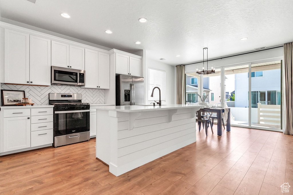 Kitchen with stainless steel appliances, decorative backsplash, a sink, a chandelier, and light wood finished floors
