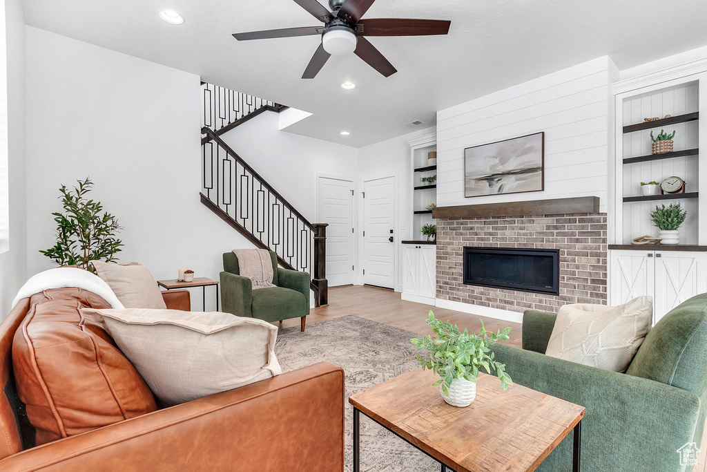 Living room with stairway, a ceiling fan, wood finished floors, built in features, and recessed lighting