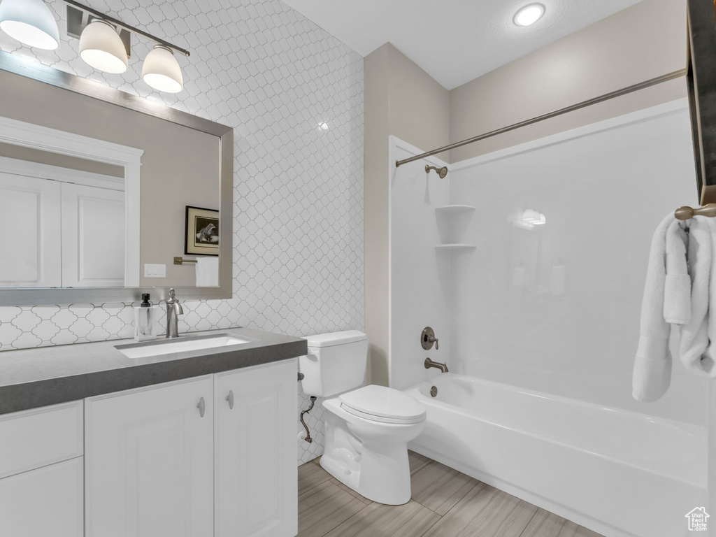 Bathroom featuring wallpapered walls, toilet, vanity, and washtub / shower combination