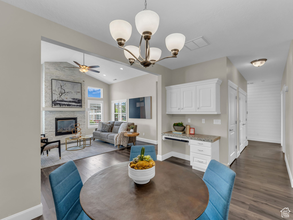 Dining area with dark wood-type flooring, baseboards, a ceiling fan, vaulted ceiling, and a stone fireplace