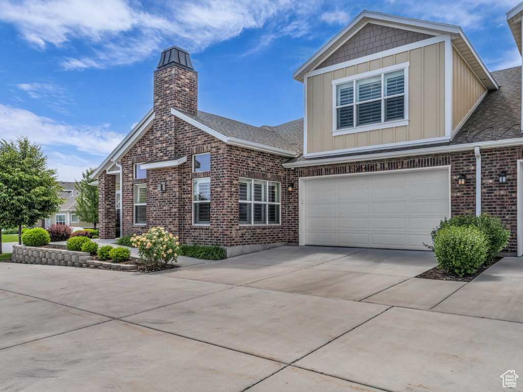 View of front of property with driveway, board and batten siding, brick siding, an attached garage, and a chimney