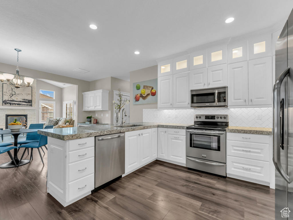 Kitchen featuring stainless steel appliances, a sink, a peninsula, glass insert cabinets, and tasteful backsplash