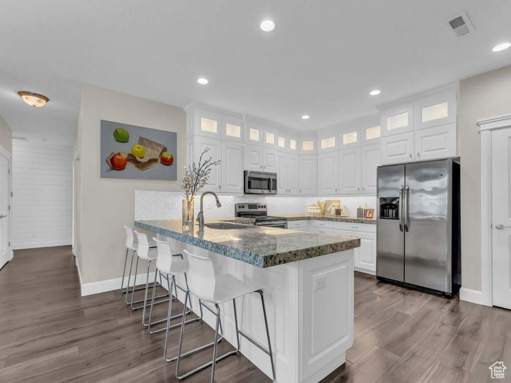 Kitchen with appliances with stainless steel finishes, a sink, a peninsula, baseboards, and white cabinets
