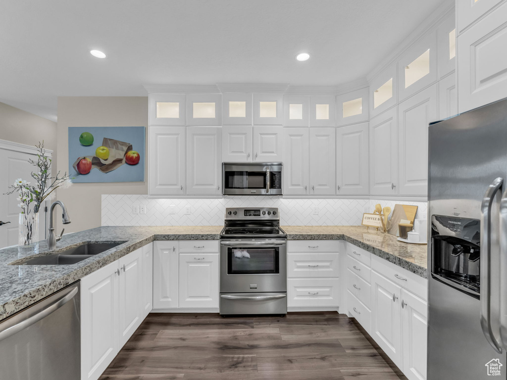 Kitchen featuring appliances with stainless steel finishes, a sink, backsplash, white cabinetry, and light stone countertops
