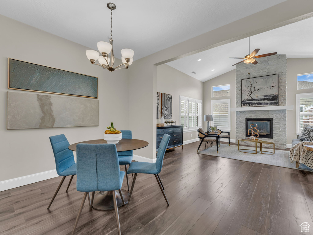 Dining area featuring lofted ceiling, baseboards, wood finished floors, a stone fireplace, and a chandelier