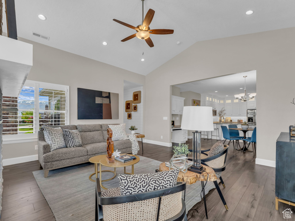 Living area with baseboards, a ceiling fan, dark wood-style flooring, lofted ceiling, and a chandelier