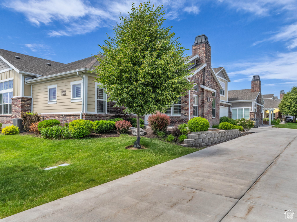 View of front facade featuring brick siding, a front lawn, a chimney, concrete driveway, and a garage
