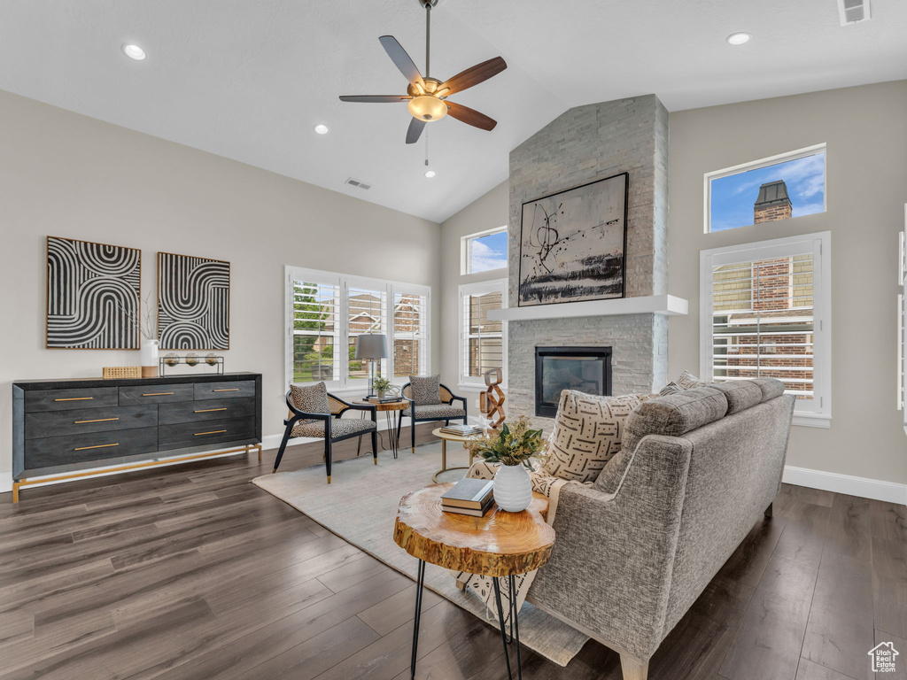Living area with ceiling fan, high vaulted ceiling, baseboards, dark wood-style floors, and a stone fireplace