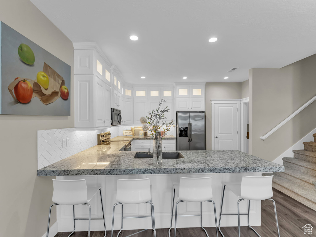 Kitchen featuring appliances with stainless steel finishes, a sink, a peninsula, dark wood-style flooring, and tasteful backsplash