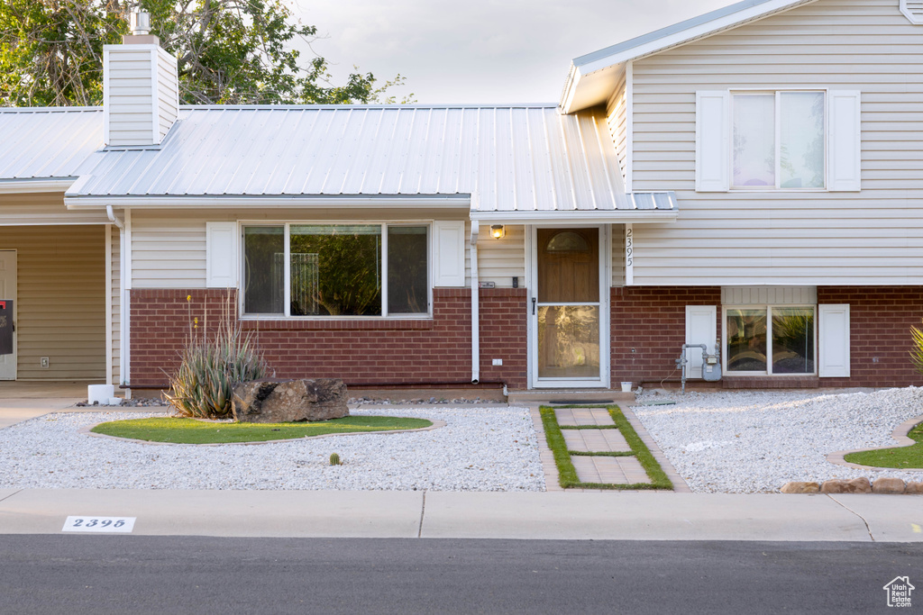 Tri-level home with brick siding, a chimney, and metal roof
