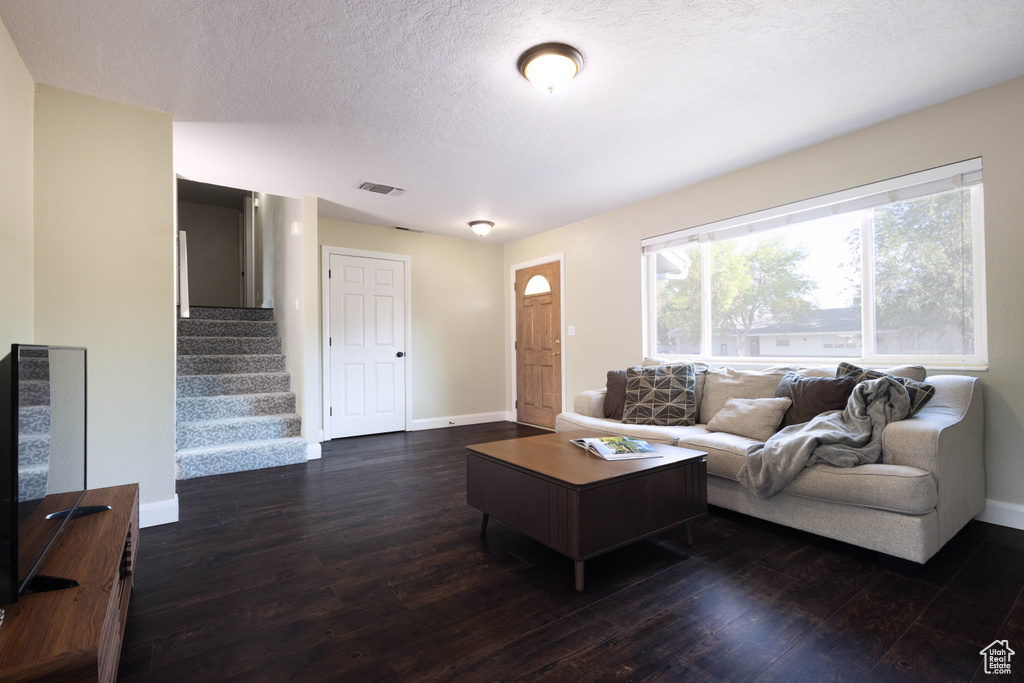 Living room featuring dark wood-type flooring, baseboards, stairway, and a textured ceiling
