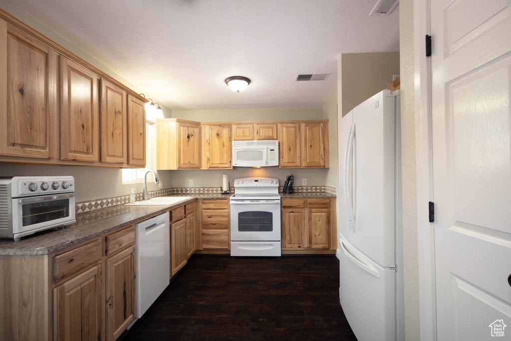 Kitchen featuring white appliances, a sink, dark wood-style flooring, and light brown cabinetry