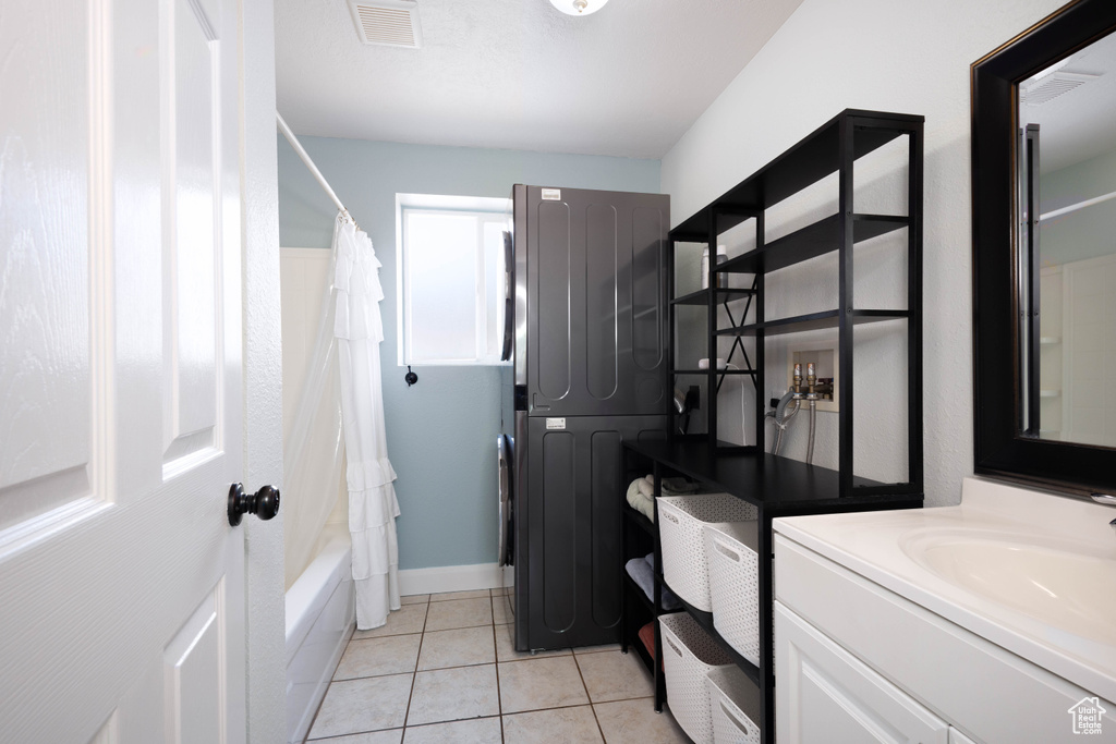 Bathroom with stacked washer / dryer, vanity, shower / bathtub combination with curtain, tile patterned flooring, and baseboards