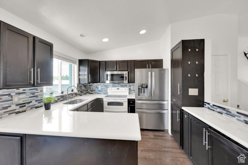 Kitchen with stainless steel appliances, a sink, tasteful backsplash, light countertops, and vaulted ceiling