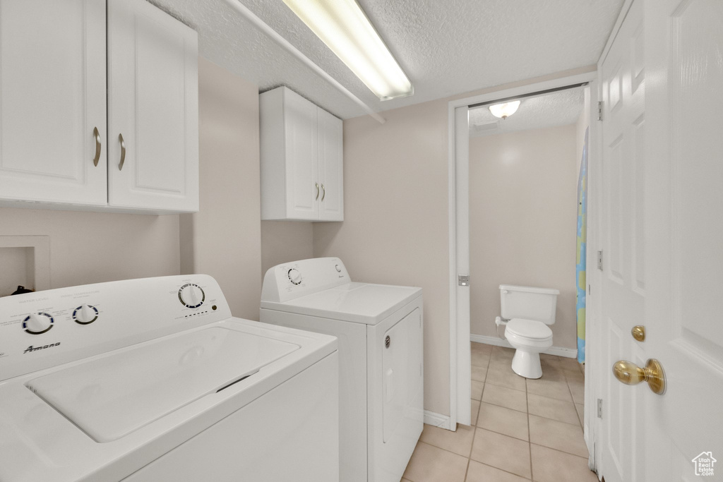 Laundry area featuring washer and dryer, cabinet space, a textured ceiling, light tile patterned floors, and baseboards