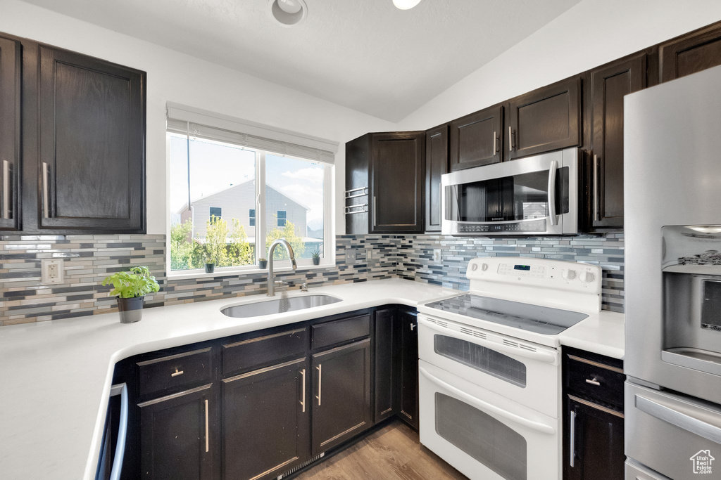 Kitchen featuring stainless steel appliances, a sink, backsplash, vaulted ceiling, and light countertops