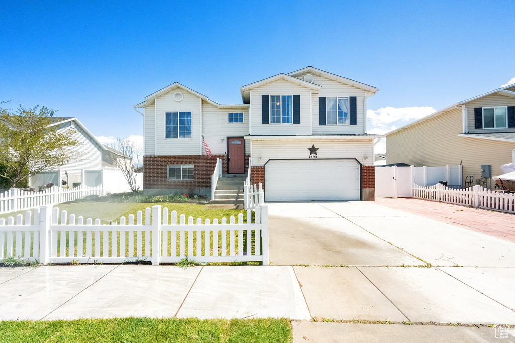View of front of home with brick siding, a garage, a fenced front yard, and concrete driveway