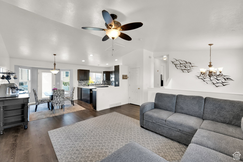 Living room with a chandelier, lofted ceiling, dark wood finished floors, ceiling fan, and baseboards