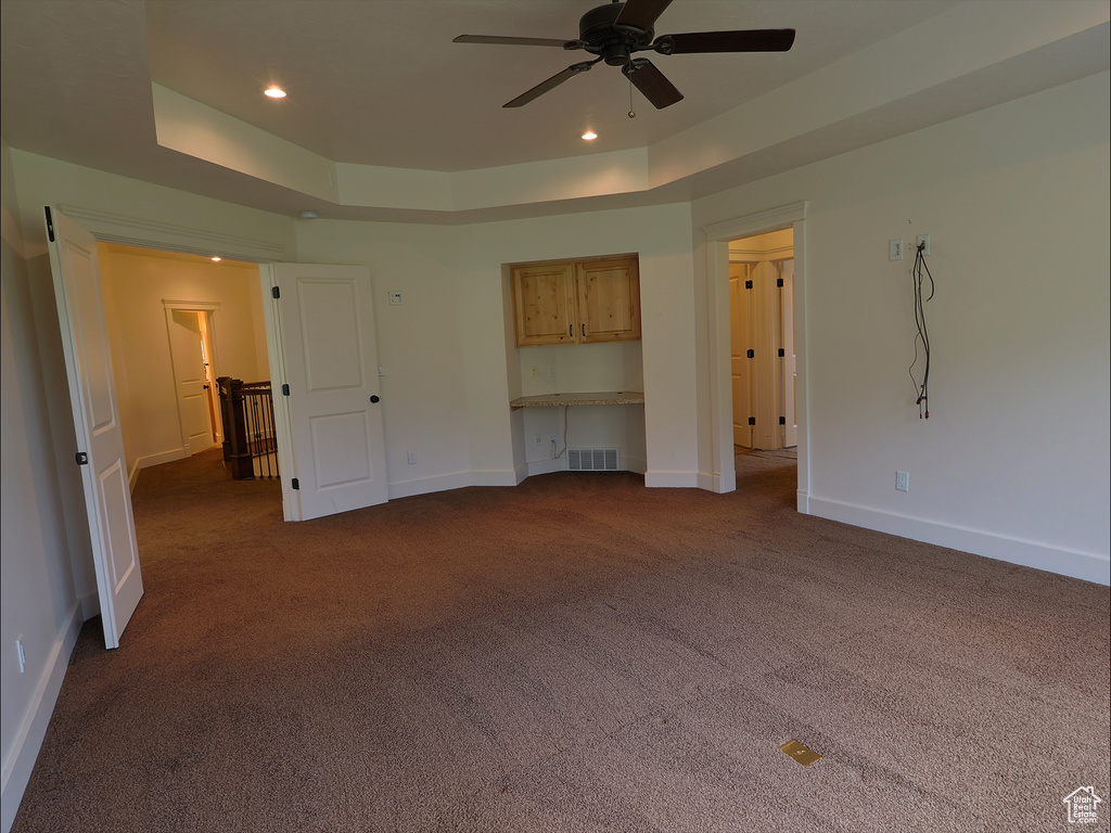 Unfurnished bedroom with a tray ceiling, dark colored carpet, baseboards, recessed lighting, and ceiling fan