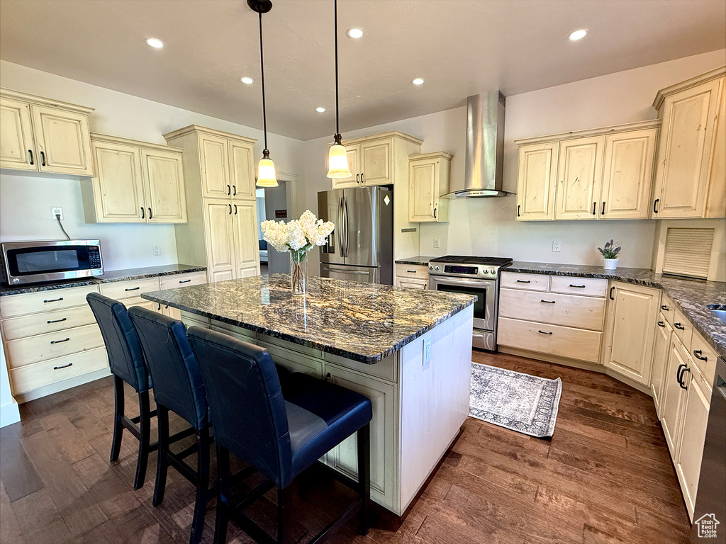 Kitchen with appliances with stainless steel finishes, wall chimney range hood, a kitchen island, cream cabinetry, and recessed lighting